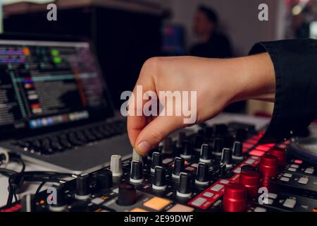 La mano del DJ sul computer portatile e la console di mixaggio che controlla impostazioni audio Foto Stock