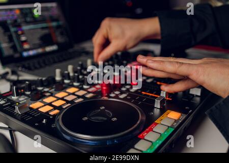 La mano del DJ sul computer portatile e la console di mixaggio che controlla impostazioni audio Foto Stock