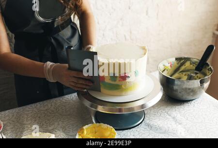 Una giovane ragazza pasticciera in grembiule grigio decora una torta in cucina. Foto Stock