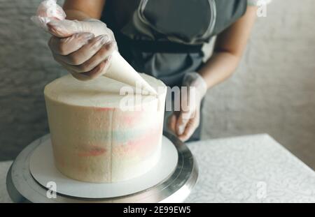 Una ragazza pasticciera fa una torta di nozze con le proprie mani e spreme la crema sugli strati della torta. Un pasticciere produce una crema rosa utilizzando un Foto Stock