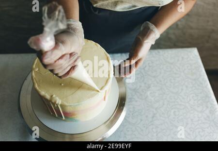 Una ragazza pasticciera fa una torta di nozze con le proprie mani e spreme la crema sugli strati della torta. Un pasticciere produce una crema rosa utilizzando un Foto Stock