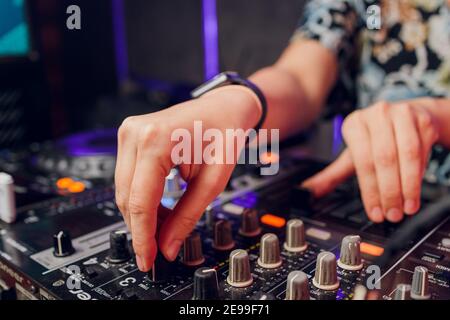 La mano del DJ sul computer portatile e la console di mixaggio che controlla impostazioni audio Foto Stock