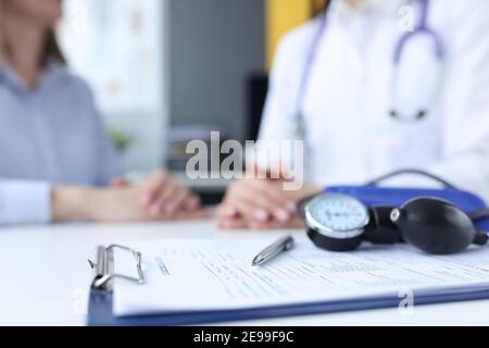 Tonometro e appunti con anamnesi medica sdraiati sul tavolo vicino medico e paziente Foto Stock