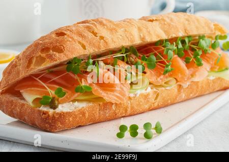 Sandwich grande con salmone, formaggio cremoso, fettine di cetrioli su tavola di cemento bianco. Foto Stock