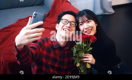 Felice giovane coppia asiatica che prende selfie. Donna con rose rosse. Foto di alta qualità Foto Stock