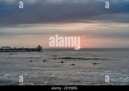 Playa Varadero, Huanchaco, al tramonto sull'oceano pacifico con alcuni surfisti in acqua e il lungo molo sullo sfondo Foto Stock