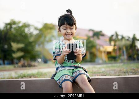 Little Girl che studia online utilizzando lo smartphone nel cortile di casa Foto Stock