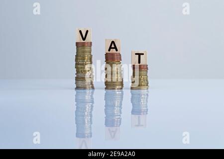 La parola "IVA" sui blocchi di legno in cima alle pile discendenti di monete in grigio. Foto concettuale della riduzione dell'imposta sul valore aggiunto, dell'economia, delle imprese e della finanza Foto Stock