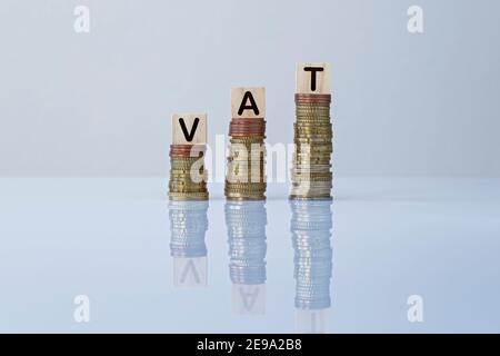 Parola 'IVA' sui blocchi di legno in cima a pile di monete ascendenti su sfondo grigio. Foto concettuale dell'aumento delle tasse, dell'economia, delle imprese e della finanza. Foto Stock