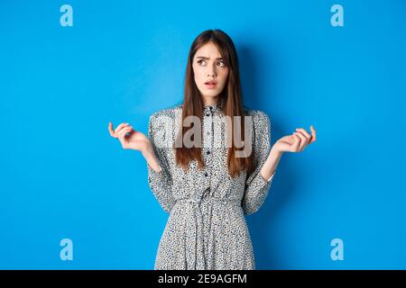 Confuso cute ragazza cant capire qualcosa, guardare via pensive e contare sulle dita, in piedi in abito contro sfondo blu Foto Stock