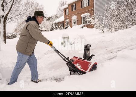 Berks County, Pennsylvania-2 febbraio 2021: Uomo anziano che usa un soffiatore di neve per liberare il marciapiede e il vialetto dopo la tempesta di neve Foto Stock