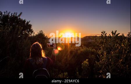 MAR DE LAS PAMPAS, ARGENTINA - 20 ottobre 2018: Giovane donna che ritrae il tramonto con il suo cellulare con un grande tramonto Foto Stock