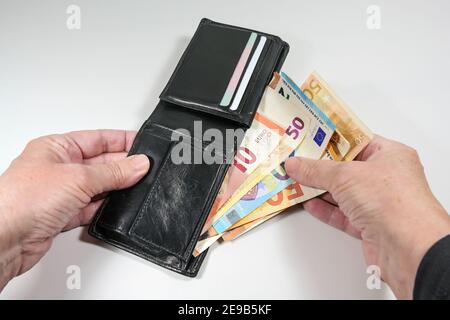 Mani che prendono varie banconote in euro da un portafoglio in pelle nera, concetto di denaro e finanza, sfondo grigio chiaro, fuoco selezionato, profondità stretta di f Foto Stock