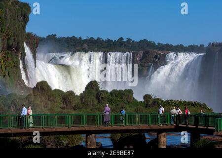 I turisti su un passaggio sopraelevato ammirano una sezione delle Cascate di Iguazu in Brasile. Sullo sfondo si trova la cascata della Gola del Diavolo. Foto Stock