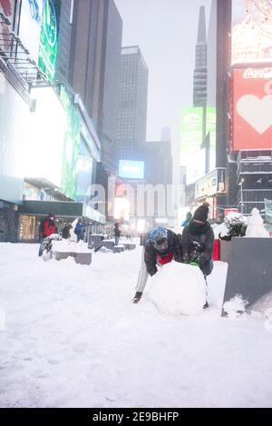 Ragazze che rotola una grande sfera di neve per costruire un Pupazzo di neve a Times Square Foto Stock