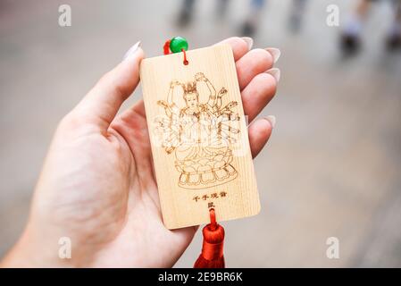 La mano della donna tiene una tavola di legno con l'immagine di un Buddha Multi-armato. Tablet è progettato per scrivere desideri o preghiere su di esso. Tradizioni asiatiche. Foto Stock