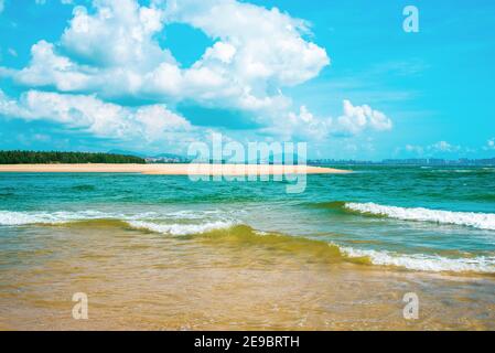Bella stagione. Spiaggia di sabbia gialla, mare azzurro e cielo blu con belle nuvole. Le onde vengono lavate fino alla riva. Isola paradisiaca di Hainan, Sanya. Foto Stock