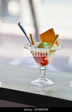 Una tazza seducente di gelato con un cucchiaio e un assortimento di wafer su un tavolo su uno sfondo fuori fuoco. Concetto di cibo dolce. Foto Stock