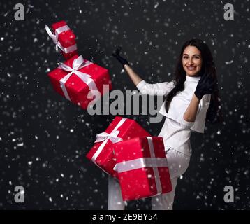 Giovane donna sorridente dottore dentista in uniforme bianca e lattice guanti con bretelle in piedi con scatole regalo di festa volanti intorno Foto Stock