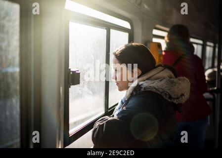 Donna turista che viaggia su un tram soleggiato giorno estivo felice sorridendo e guardando fuori dalla finestra del treno mentre si passa città con altri passeggeri Foto Stock