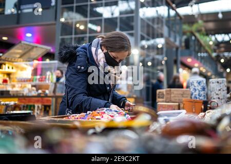 Donna che acquista indossando maschera protettiva nera che guarda attraverso il mercato riporre gli oggetti al sicuro in un negozio all'aperto durante le limitazioni pandemiche Foto Stock