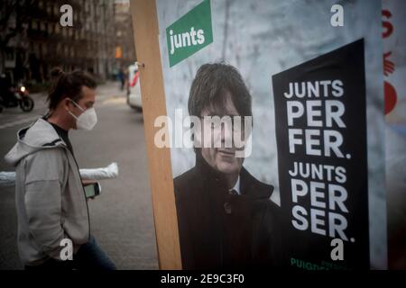 L'uomo che indossa una maschera facciale passa accanto a un poster della campagna Junts per Catalunya, che mostra l'ex presidente catalano e membro DEL Parlamento europeo CARLES PUIGDEMONT. La regione autonoma della Catalogna terrà le elezioni il prossimo 14 febbraio tra le preoccupazioni per la crisi sanitaria del coronavirus. Foto Stock