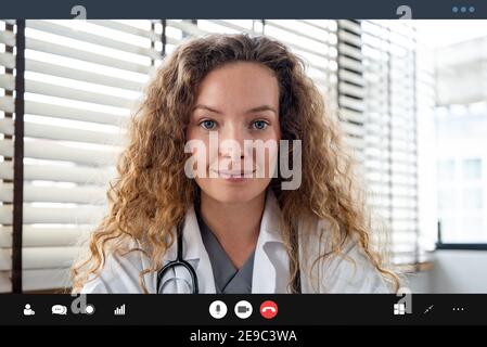 Dottore femminile che guarda la telecamera mentre si effettua una videochiamata con i concetti del servizio di consulazione medica domestica online per il paziente Foto Stock