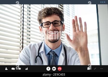 Giovane medico maschile agitando la mano saluto paziente online tramite videochiamata, concetti di servizio di consulenza medica a casa Foto Stock