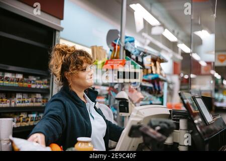 Donna che lavora come cassiere in un negozio di alimentari. Cassa femminile che assiste i clienti al check-out del negozio. Foto Stock