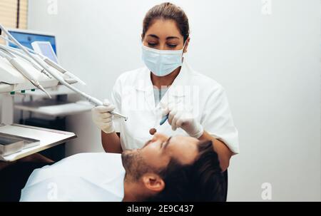 Dentista femminile che esamina i denti di un uomo in clinica dentale usando gli attrezzi dentali. Dentista che ispeziona i denti di un paziente maschio. Foto Stock