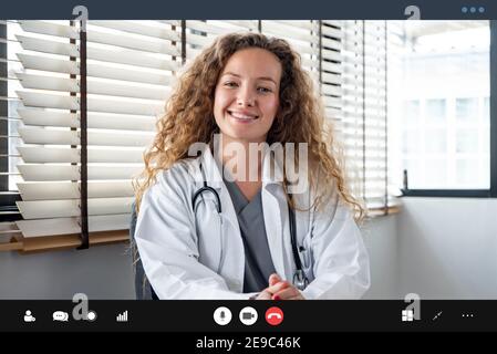 Sorridente allegro caucasico donna medico guardando la fotocamera mentre avendo riunione in linea con paziente, casa medica consulazione servizio di videochiamata c Foto Stock