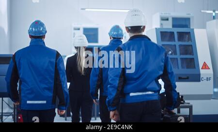 Capo di progetto femminile, team di ingegneri, lavoratori, sicurezza, Ispettore di controllo indossare i cappelli duri camminare attraverso la fabbrica industriale. Struttura con Foto Stock