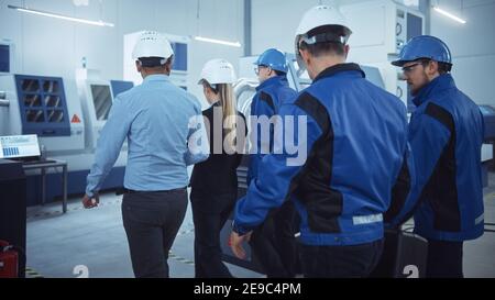 Capo di progetto femminile, team di ingegneri, lavoratori, sicurezza, Ispettore di controllo indossare i cappelli duri camminare attraverso la fabbrica industriale. Struttura con Foto Stock