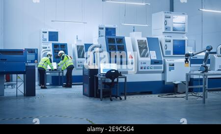 Capo ingegnere e Project Manager indossare giubbotti di sicurezza e cappelli duri lavorare su computer, parlare, ottimizzare la linea di produzione. In primo piano: Industria 4.0 Foto Stock