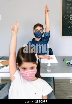 Studenti con maschere che alzano le mani a scuola Foto Stock