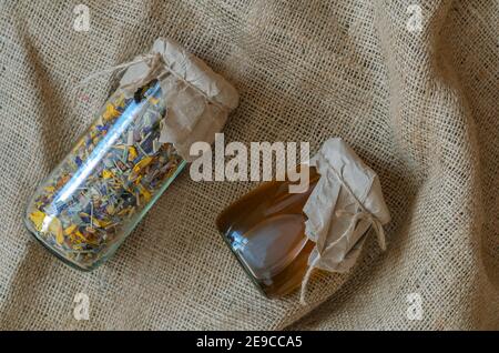 Erbe e medicina alternativa concept.erbe medicinali essiccati erbe e miele di api. Tè di fiori secchi e miele liquido crudo in vasetti di vetro su burlap. Foto Stock