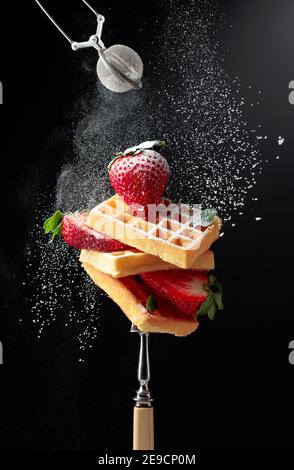 Waffle con fragole fresche e succose cosparse di polvere di zucchero su sfondo nero. Foto Stock