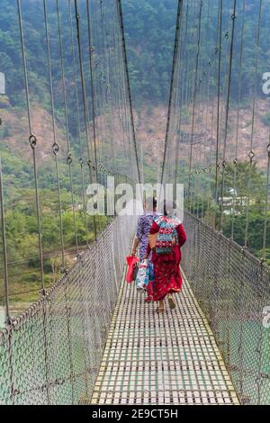 Le donne che attraversano la sospensione ponte sopra il fiume Trishuli in Nepal Foto Stock