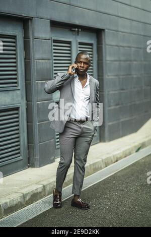 Colpo verticale di un bel maschio africano sicuro in un suit che parla al telefono Foto Stock