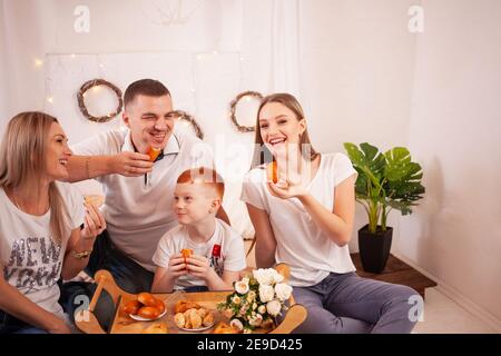 Una famiglia felice sorride e mangia dolci. Torte e dolci deliziosi con ciliegie, funghi. Papà, mamma e due bambini hanno la prima colazione, pranzo sulla b Foto Stock