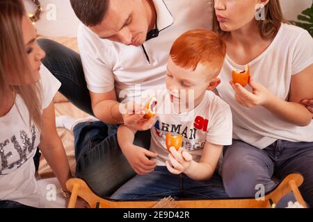 Una famiglia felice sorride e mangia dolci. Torte e dolci deliziosi con ciliegie, funghi. Papà, mamma e due bambini hanno la prima colazione, pranzo sulla b Foto Stock