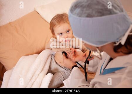 Il medico ascolta il cuore e i polmoni di una bambina a casa. Bambino malato, quarantena domestica, coronavirus, covid. Foto Stock