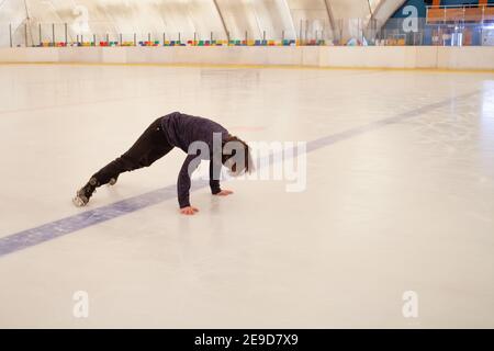 Un uomo mascherato cade sul ghiaccio. L'uomo cadde sui pattini. Pista di pattinaggio interna. Foto Stock