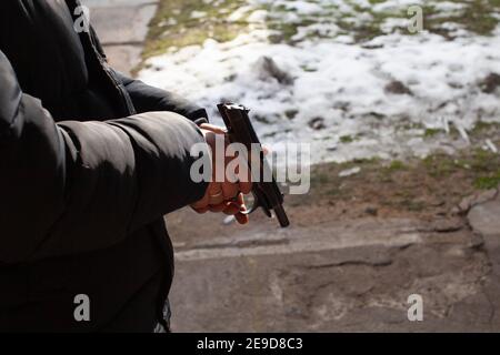 Un uomo ricarica una pistola. Inverno, fuori porta, raggio di tiro. Omicidio, pericolo, armi da fuoco. Neve a terra Foto Stock