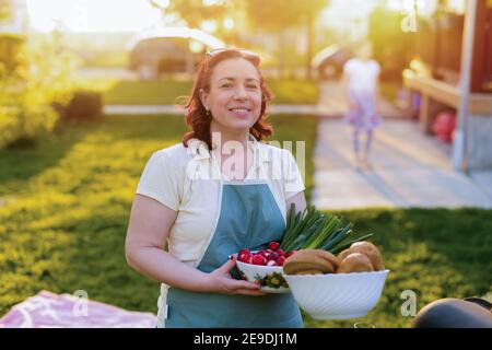 Immagine della bella donna di mezza età che tiene il cibo nelle sue mani. Pranzo in famiglia in cortile. Foto Stock