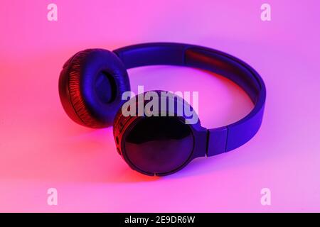 Eleganti cuffie wireless nere illuminate con coloratissima luce al neon su sfondo astratto isolato. Concetto di tecnologia moderna con spazio di copia Foto Stock
