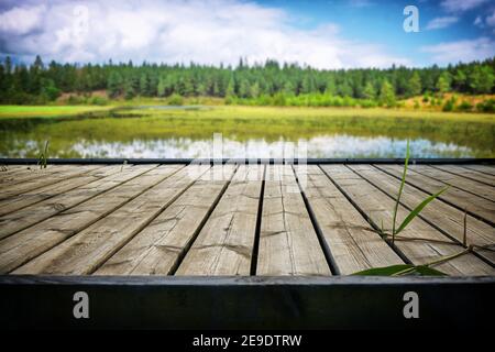 Molo in legno con tavole su un idilliaco lago nella estate con canne in crescita sul palco Foto Stock