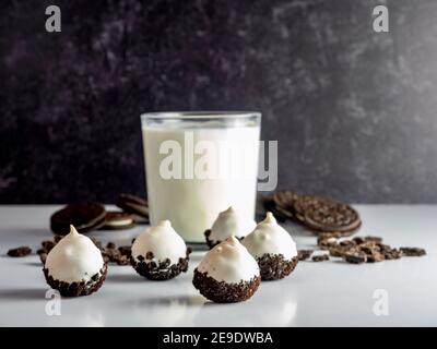 Biscotti e palle di torta alla crema, tartufo come dessert, con un bicchiere di latte fresco e biscotti sandwich sullo sfondo, su un bancone bianco con un nero Foto Stock