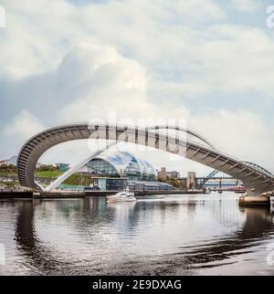 Barca di lusso sotto il moderno ponte aperto sopraelevato Gateshead Millennium Bridge Riflettendo in acqua che passa del fiume Tyne in verticale Newcastle panorama cielo Foto Stock