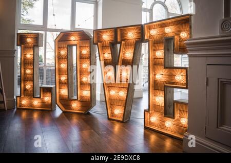 Matrimonio grande alto amore maiuscolo lettere legno rustico illuminato su pista da ballo di bella sala cerimonia che illumina arancione Foto Stock